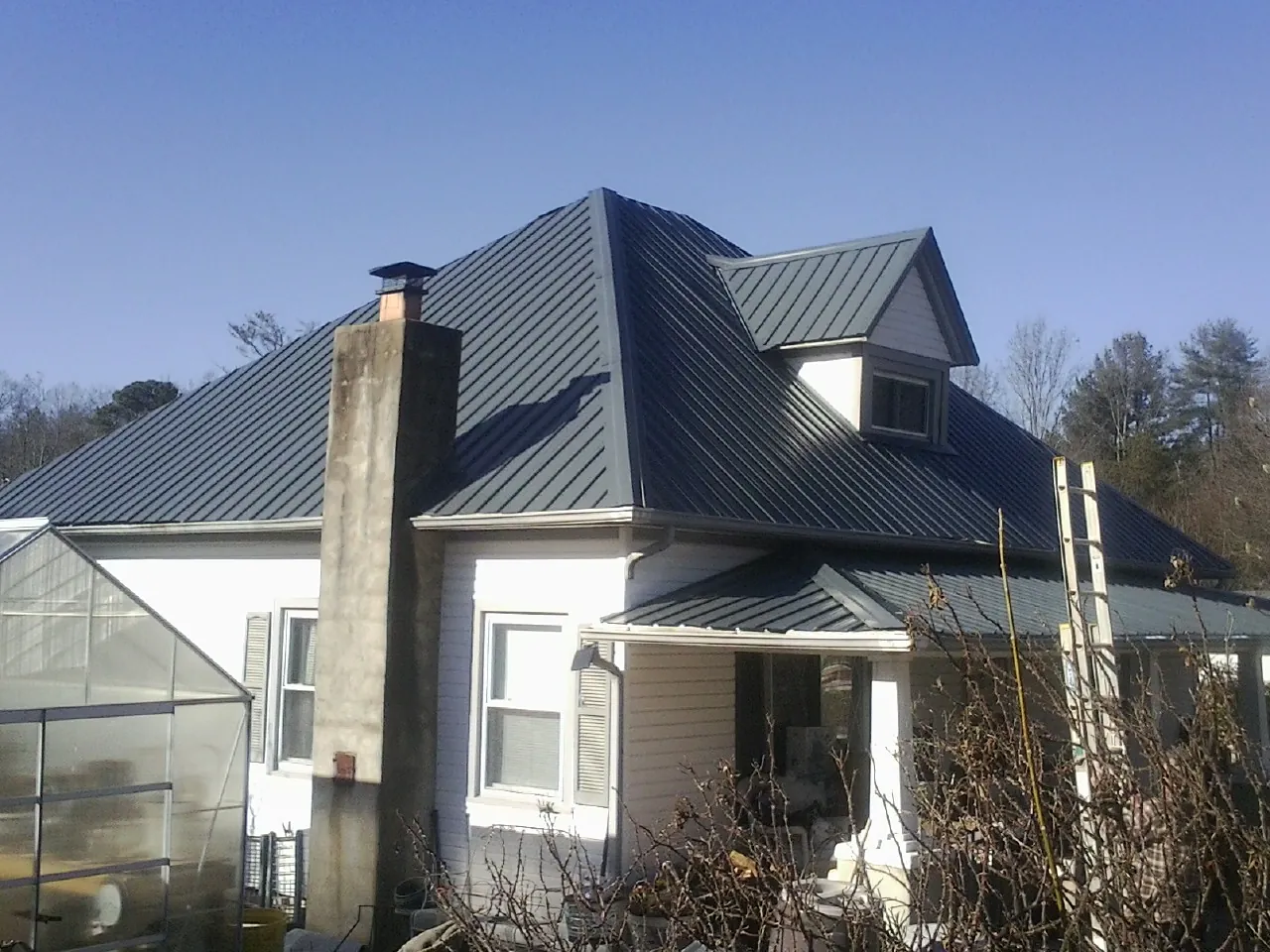 Dark blue standing seam metal roof on a white farmhouse with dormer in Camp Douglas