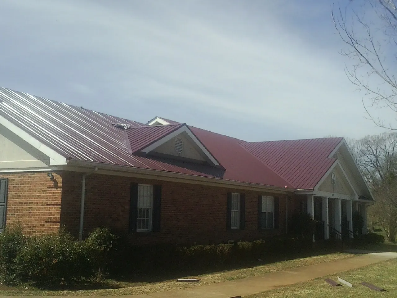 Red metal roof with gabled entries on a long brick building, from a Hail Damage Roof Repair job in Camp Douglas