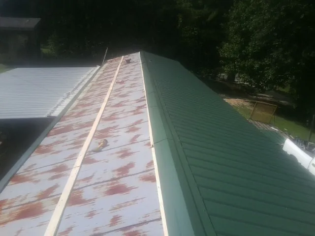 Old rusted panels beside newly installed green metal roofing — Wind Damage Roof Repair by Roofing Brothers in Camp Douglas