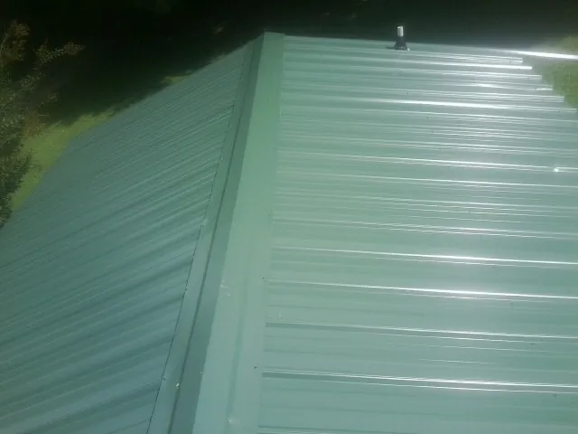 New green metal panels meeting at the ridge of a roof — Flat Roof Repair work by our crew in Camp Douglas