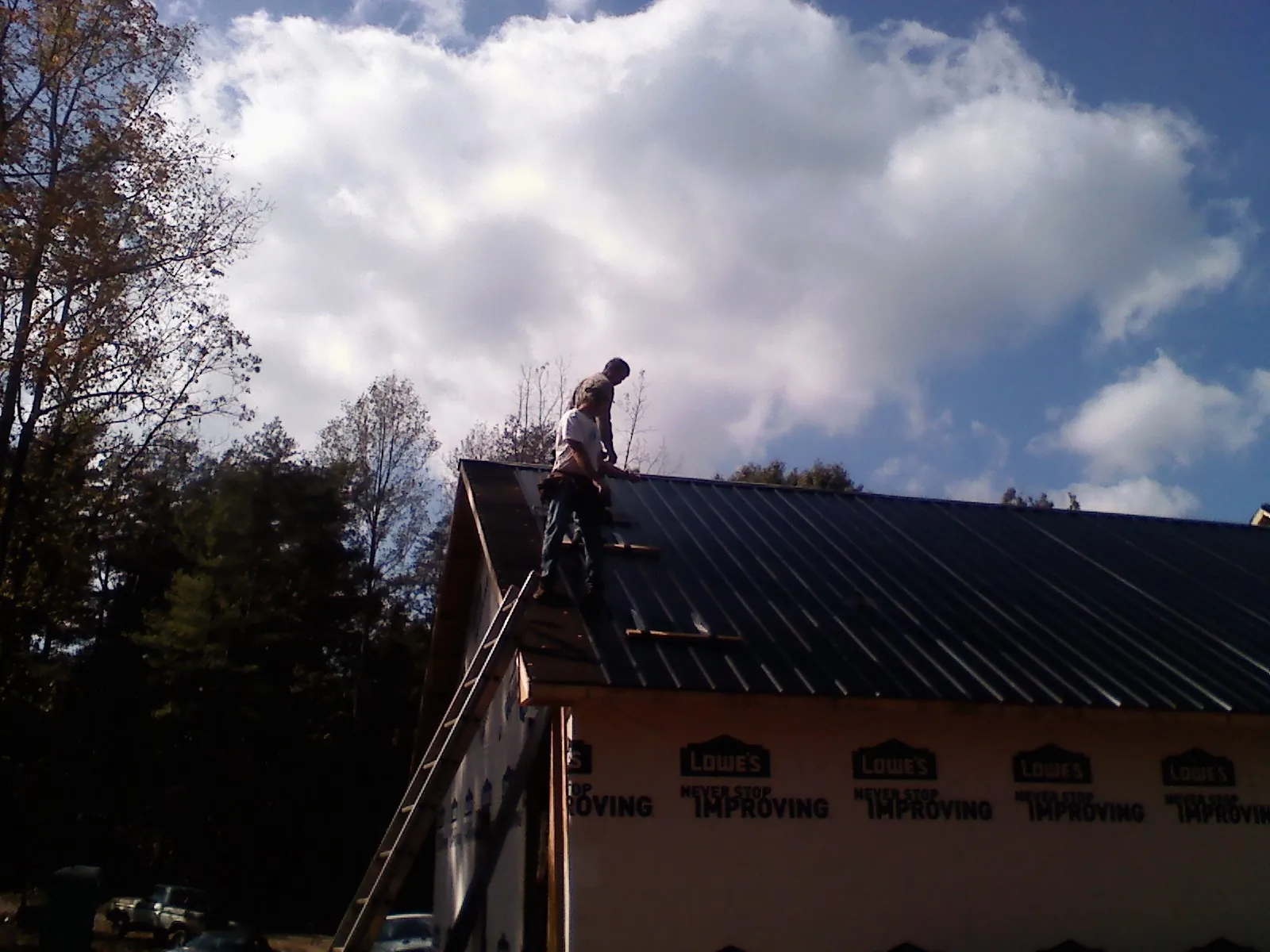 Roofer fastening dark metal panels high against a cloudy sky, from a Roof Inspection job in Camp Douglas