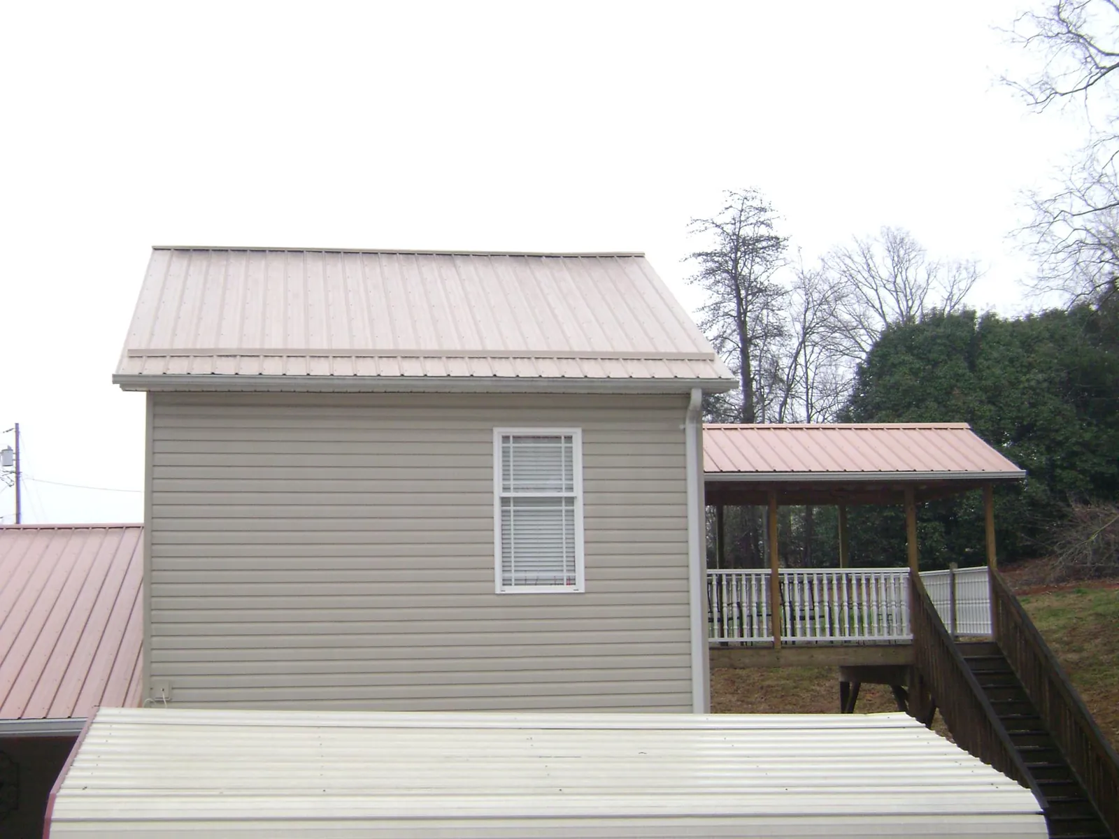 Tan metal roofs on a two story addition and attached porch, from a Roof Replacement job in Camp Douglas