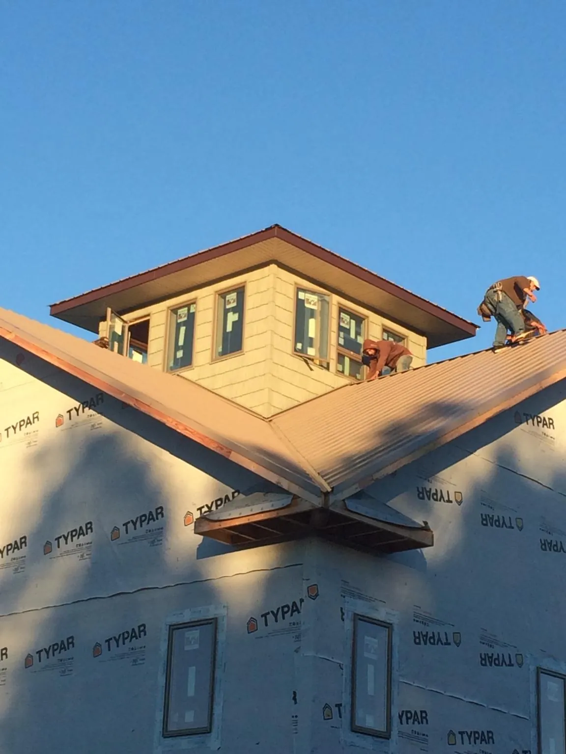 Roofers working around a rooftop cupola on a new metal roof at sunset — Roof Waterproofing in Camp Douglas by Roofing Brothers